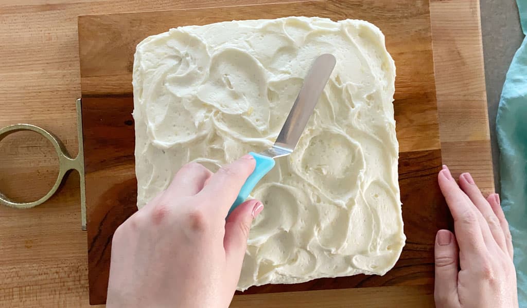 Lemon Cake Step 13- Spread Icing spreading lemon icing on cake