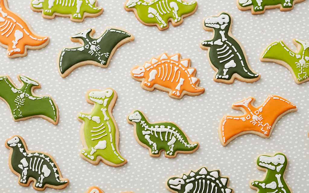 dinosaur-cookies sugar cookies shaped like dinosaurs and decorated with colored green and orange royal icing