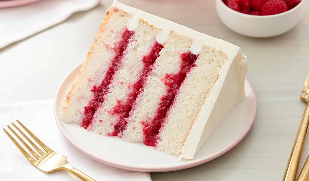 frozen-raspberries--cake--in-post raspberry filled cake frosted with white buttercream frosting on a plate