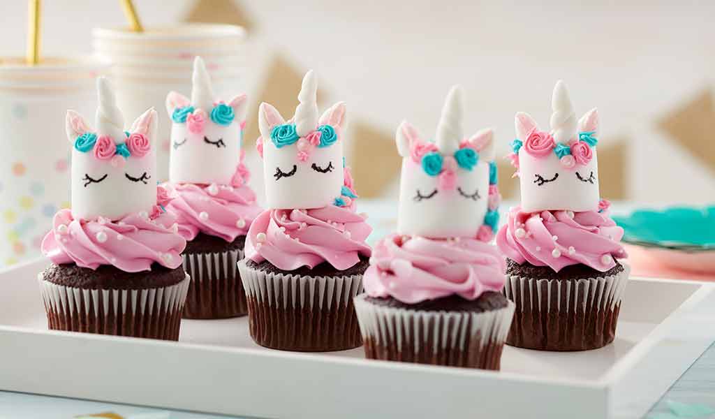 chocolate cupcakes with pink buttercream frosting and marshmallows decorated as unicorns