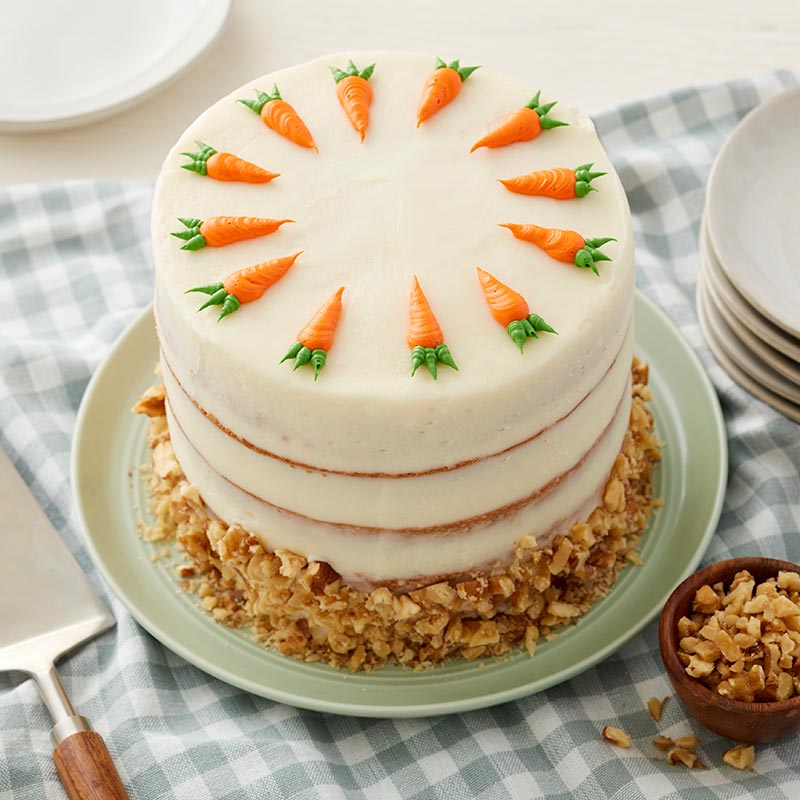Carrot-Cake-Recipe-Blog-Post Round carrot cake with cream cheese frosting and walnuts. Topped with buttercream piped carrots
