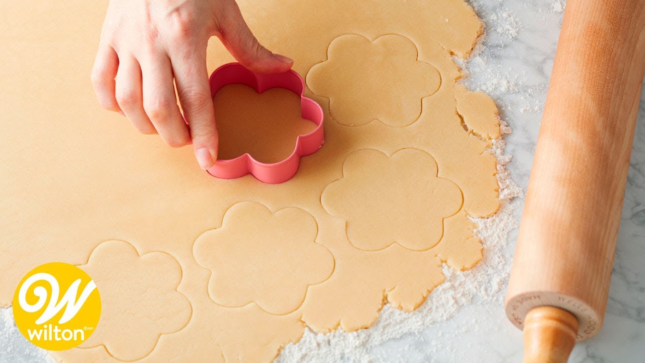 A picture of a baker using a floral shaped cutter to cut recently rolled cookie dough