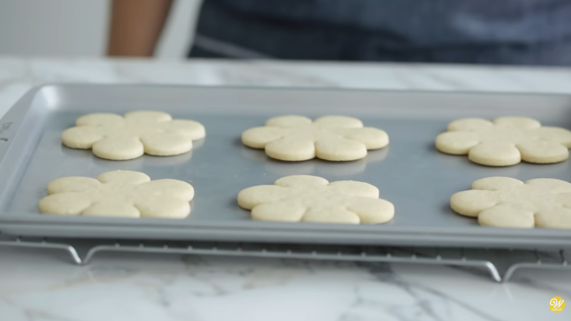 recently-baked-cut-out-cookies-cooling-off A picture of a batch of recently baked cut-out sugar cookies on a marble kitchen counter still in the baking sheet as it's resting on a cooling grid